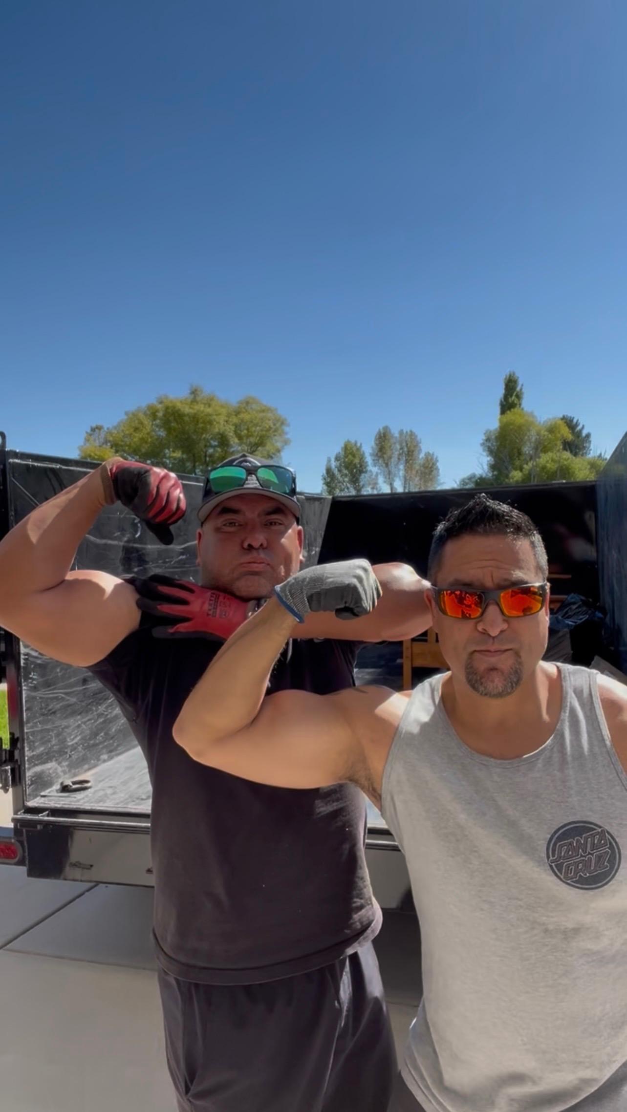 Yolked Junk Removal owners flexing in front of a trailer